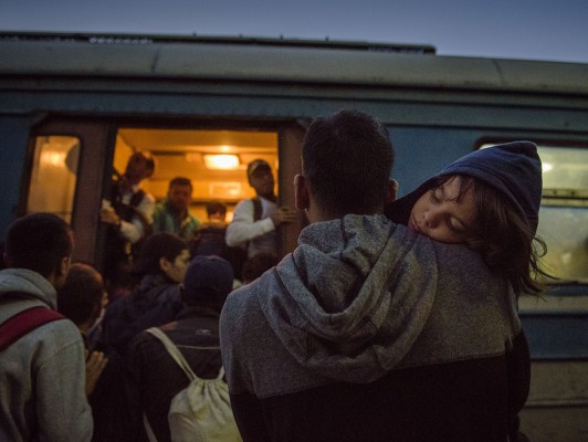 Një refugjat po mban fëmijën e tij të fjetur ndërsa përpiqet të hyjë në një tren të mbingarkuar në Tabanocvë | Photo by: Elena Geroska