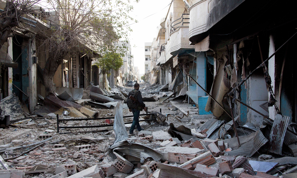 Një luftëtar kurd po ecën përmes rrënojave të Kobanit në Siri më 19 nëntor 2014. Kurdët po luftojnë me ashpërsi forcat e Shtetit Islamik, ku militojnë edhe xhihadistët shqiptarë. (AP Photo/Jake Simkin)