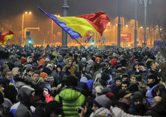 Turma njerëzish valvitin flamurin rumun jashtë godinës qeveritare. Foto: (AP Photo/Vadim Ghirda)