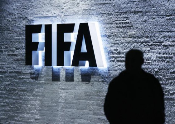 Një burrë qëndron përpara logos së FIFA-s në selinë në Zyrih, Zvicër. (Steffen Schmidt/Keystone via AP, File)