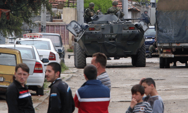 Civilët po qëndrojnë pranë një autoblinde të vendosur në një lagje të Kumanovës më 9 maj 2015. (AP Photo/Radovan Vujovic)