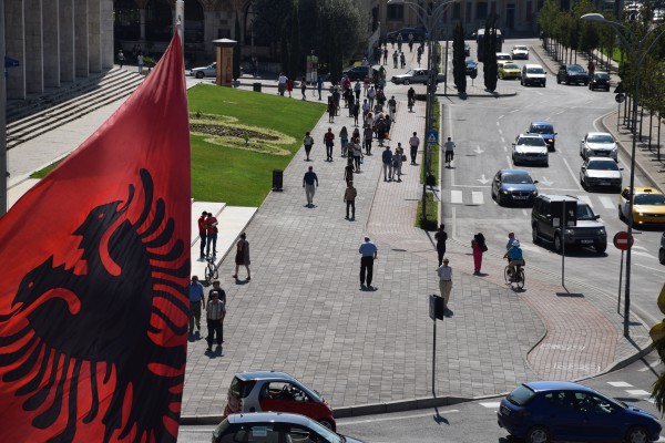 Një flamur shqiptar valvitet teksa në sfond duken kalimtarët në Sheshin Skënderbej, Tiranë. Foto: Ivana Dervishi | BIRN