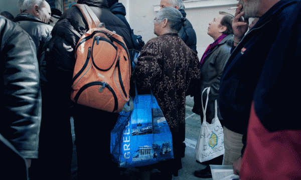 Një grua e moshuar po mban një çantë me stampën e Partenonit të lashtë ndërsa pret në rradhë bashkë me të tjerët para një qendre shpërndarje supe të drejtuar nga kisha në qendër të Athinës më 19 mars 2015. (AP Photo/Petros Giannakouris)