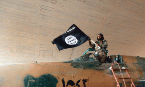 Një foto pa datë e publikuar më 27 gusht 2014 nga Qendra e Medias e Raqas të grupit Shteti Islamik. Një luftëtar i IS ngre flamurin e zi mbi një avion ushtarak të kapur nga forcat qeveritare. Foto: (AP/Shteti Islamik)