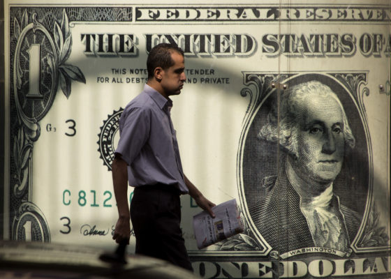 An Egyptian man walks past a poster showing a U.S. dollar outside an exchange office in Cairo, Egypt, Thursday, Nov. 3, 2016. Egypt has devalued its currency by 48 percent, meeting a key demand set by the International Monetary Fund in exchange for a $12 billion loan over three years to overhaul the country's ailing economy. The much heralded decision by the Egyptian Central Bank to devalue the pound followed a sharp and sudden decline this week in the value of the dollar in the unofficial market, plunging from an all-time high of 18.25 pounds to around 13 to the U.S. currency. (AP Photo/Amr Nabil)