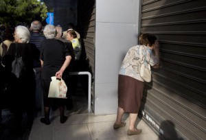 Një grua e moshuar sheh përmes qepenave të mbyllura të një banke. Pensionistët zakonisht marrin pensionet e tyre në fund të muajit, por bankat qëndruan të mbyllura sot dhe pritet të qëndrojnë të mbyllura për të paktën një javë. (AP Photo/Petros Giannakouris)
