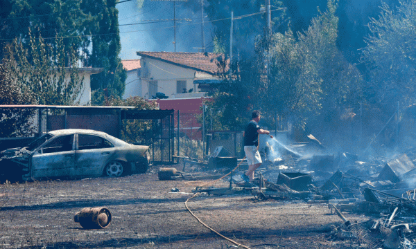 Një burrë po hedh ujë pranë një makine të djegur në fshatin Asini më 20 korrik 2015. (AP Photo/Vangelis Bougiotis)