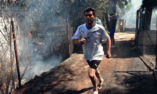 Një banor po vrapon ndërsa zjarri i afrohet një shtëpie në fshatin turistik Asini në jugperëndim të Athinës më 20 korrik 2015. (AP Photo/Vangelis Bougiotis)