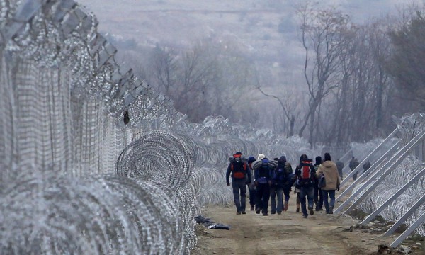 Refugjatë dhe migrantë që hynë në Maqedoni nga Greqia ilegalisht po ecin mes dy rreshtave me gardh të ndërtuar përgjatë kufirit mes dy vendeve më 29 shkurt 2016. (AP Photo/Boris Grdanoski)