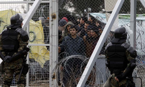 Refugjatë dhe migrantë po qëndrojnë pas gardhit me tela me gjemba pasi nuk ia dolën të hyjnë në Maqedoni nga ana greke e kufirit pranë qytezës Gevgelija të hënën më 29 shkurt 2016. Maqedonia ka kufizuar numrin e refugjatëve që hyjnë në këtë vend me numrin e atyre që kalojnë në Serbi si pasojë e kufizimeve domino të vendosura nga Europa perëndimore dhe veriore deri në jug. (AP Photo/Boris Grdanoski)