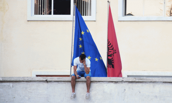 Një i ri është përqendruar te celulari i tij teksa pas i valëviten flamuri i Bashkimit Europian dhe ai i Shqipërisë, Tiranë, shtator 2015. Foto: Ivana Dervishi/BIRN.